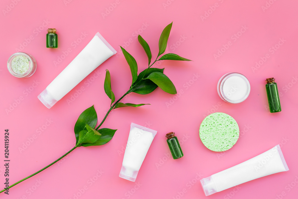 Cosmetics for skin care with natural ingredients. Eco cosmetics. Cream, lotion, oil, tonic near young green leaves on pink background top view Cosmetics for skin care with natural ingredients. Eco cosmetics. Cream, lotion, oil, tonic near young green leaves on pink background top view