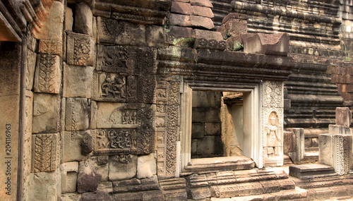 Carved stone wall with window. Ancient bricks decorated with beautifully carved details of plants, flowers, animals, people and religious figures. Angkor Thom Baphuon Temple Cambodia, Asia photo