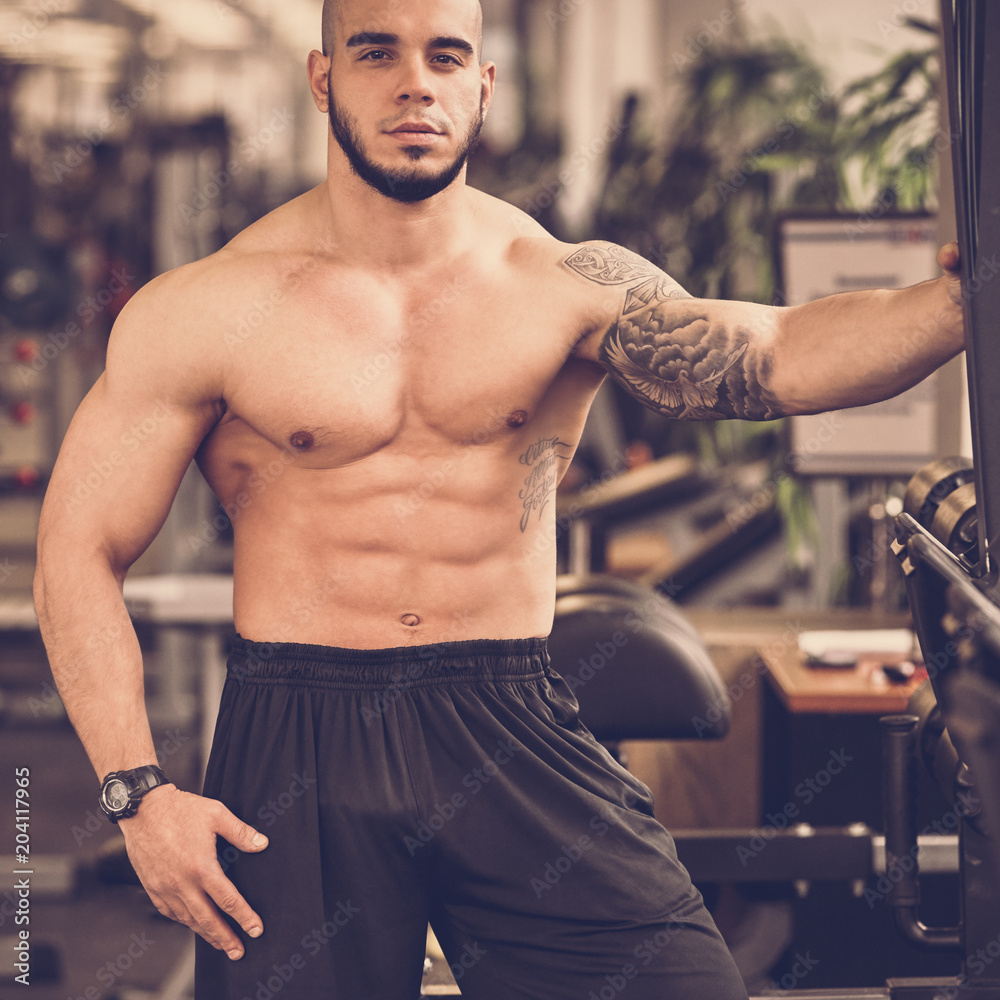 Young handsome sporty muscular man posing in gym, image with warm vintage toning