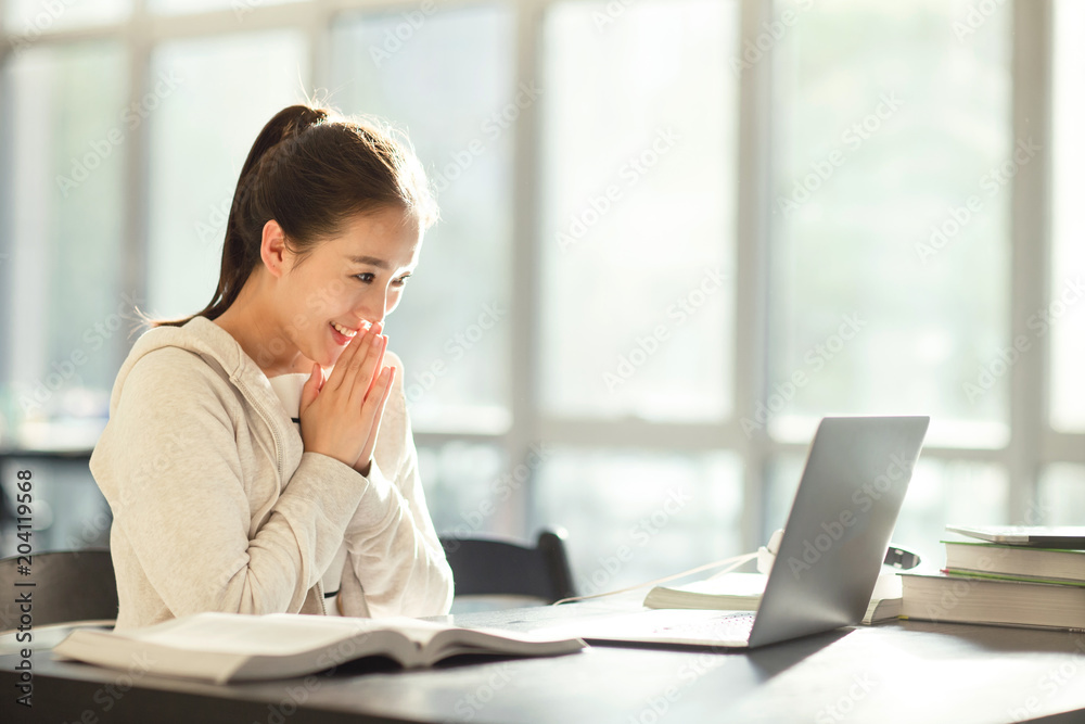 Smiling young student looking at laptop while sitting in a classroom Smiling young student looking at laptop while sitting in a classroom