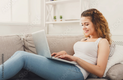 Young girl with laptop sitting on beige couch © Prostock-studio