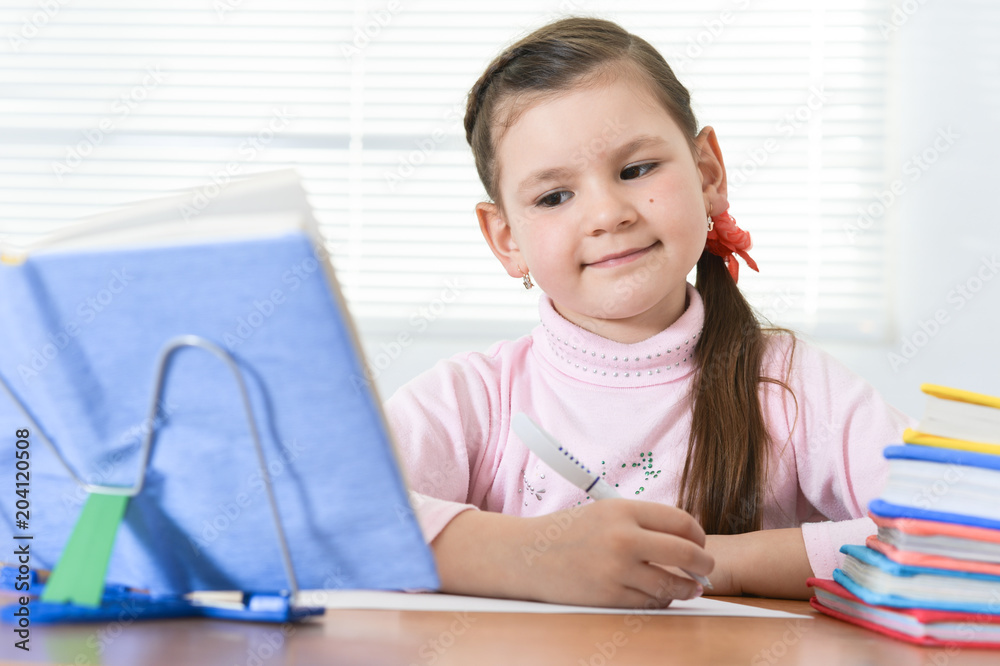 Cute schoolgirl sitting at table and doing homework at home Cute schoolgirl sitting at table and doing homework at home