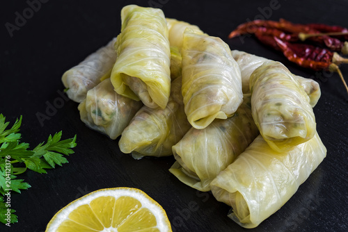 Delicious homemade stuffed cabbage leaves (the traditional dolma of the mediterranean cuisine) on black dish with parsley, red peppers and lemon