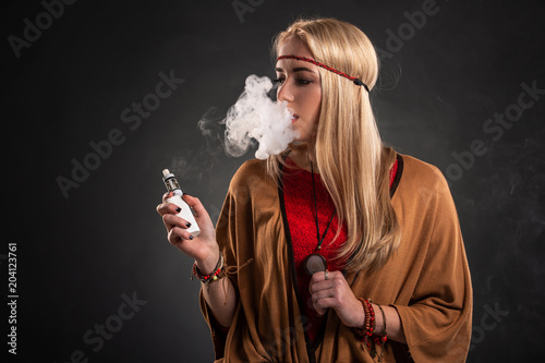 Portrait of sexy young hipster smoking vaping girl. The woman is dressed in the style of a boho. Vapor concept. Vaping e-Cigarette.