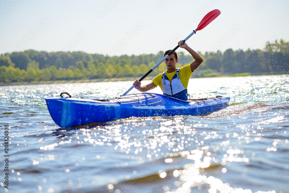 Naklejka premium Young Professional Kayaker Paddling Kayak on River under Bright Morning Sun. Sport and Active Lifestyle Concept