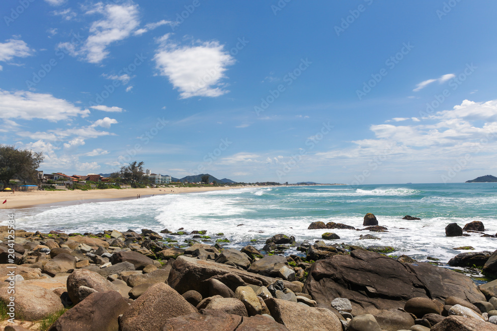 View of beach with rocks in the foreground on sunny day.