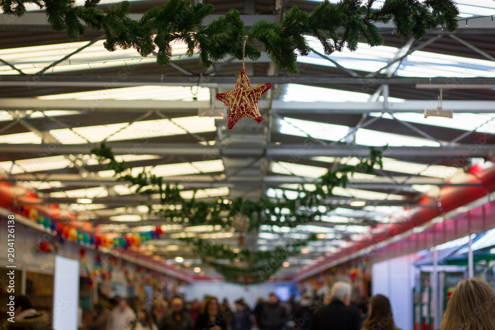 People visiting different stands on street market on Christmas season with star decoration and ribbons hanging from roof top