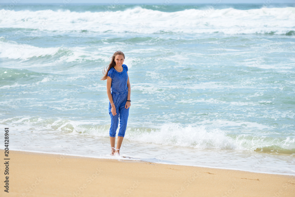 Beautiful smiling young girl in blue walking on the beach on vacation Beautiful smiling young girl in blue walking on the beach on vacation