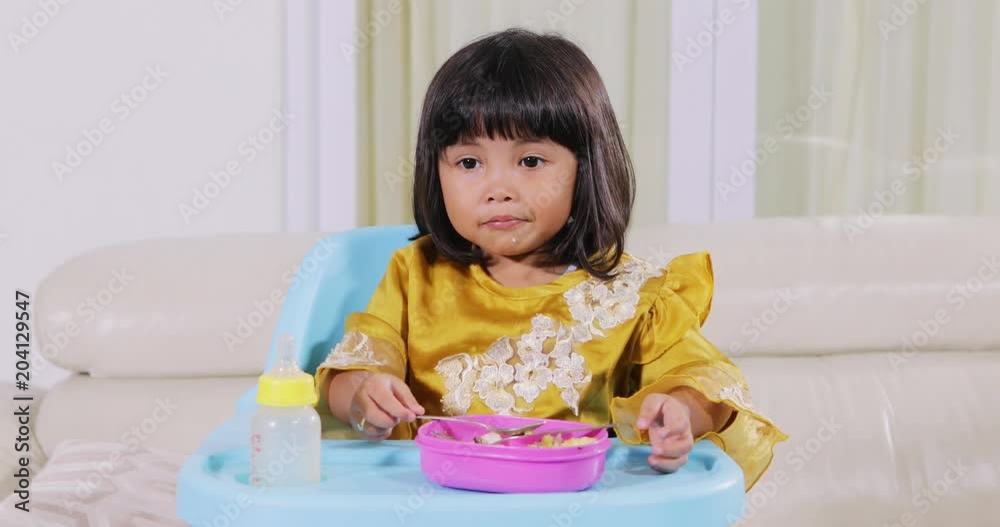 Cute little muslim girl having lunch while sitting on highchair in dining room at home. Shot in 4k resolution