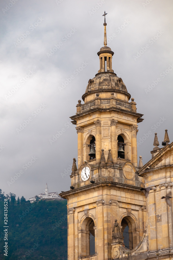 Bell tower with clock of the cathedral in the Plaza Simón Bolívar with church of Monserrate in the mountain in the background.Bogota. Colombia .