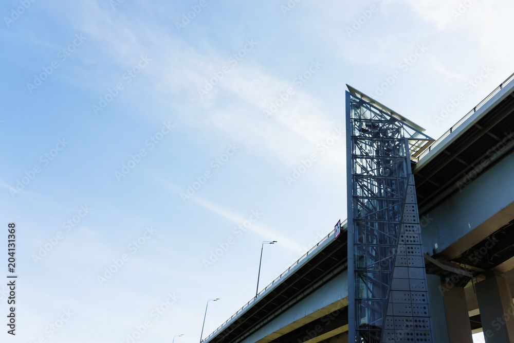 The glass elevator shaft with metal partitions on the street adjoins the bridge. The glass elevator shaft with metal partitions on the street adjoins the bridge.