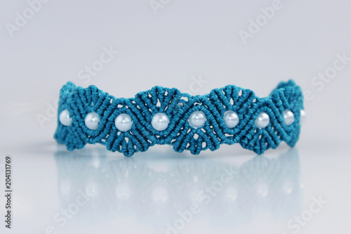 turquoise bracelete with white beads for the hand from waxed thread in the technique of macrame on a white background