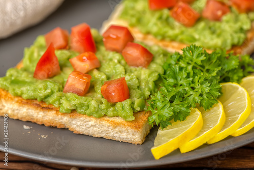close up of sandwiches with latin american mexican sauce guacamole avocado and white bread toast decorated chopped tomatoes, sliced lemon on plate, vegetarian food