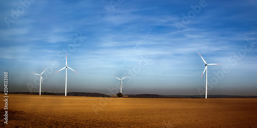 Wind machines among fields against bright sky photo