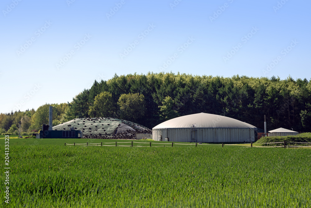biogas plant for renewable energy in a field in front of a forest, blue sky, copy space