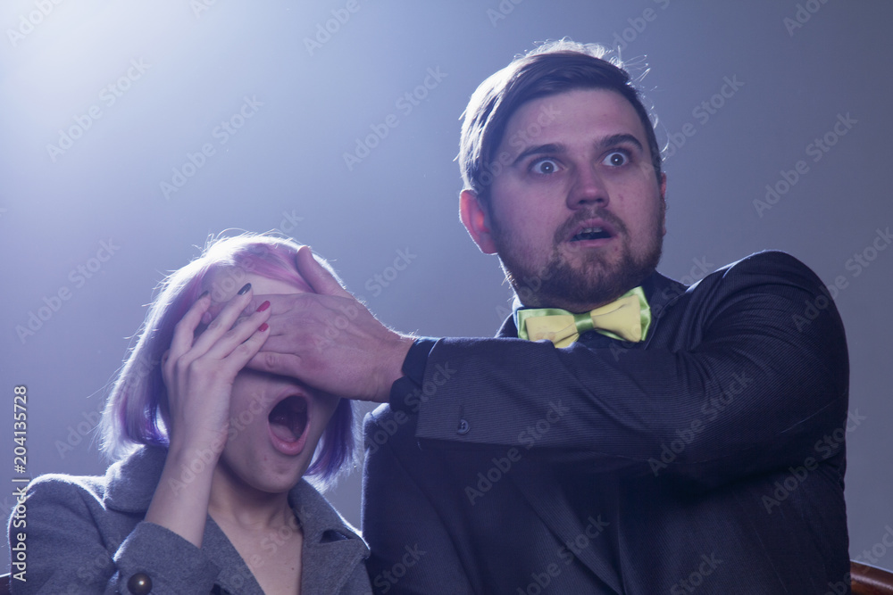 Fototapeta premium Shocked couple in love scared while watching horror scary film video movie in cinema