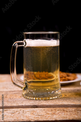 On the wooden table is a mug with a light beer. In the background is a plate with crispy croutons. Close-up.