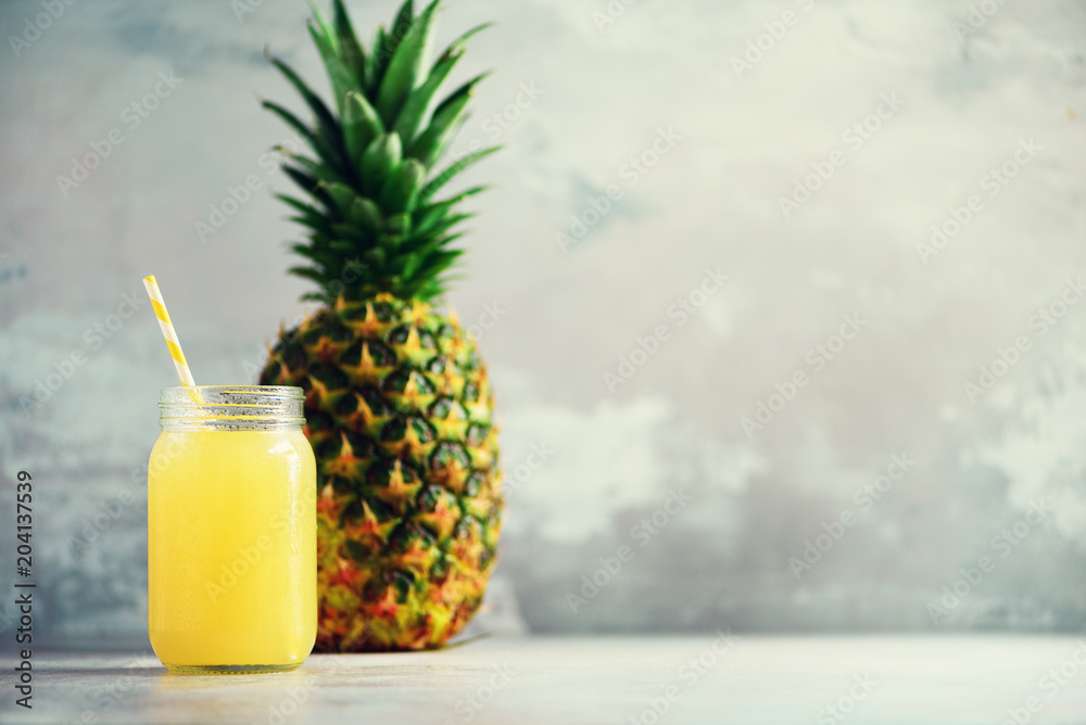 Glass bottle of pineapple juice and whole fruit on gray background with copy space. Summer, holiday concept. Raw, vegan, vegetarian, clean eating diet.