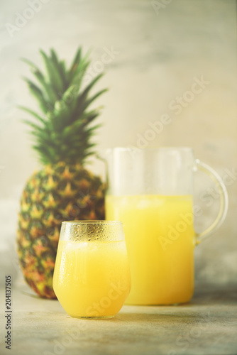 Pineapple juice in glassware and whole pineapple fruit on gray background. Copy space, sunlight effect. Summer, holiday concept. Raw, vegan, vegetarian, clean eating diet.