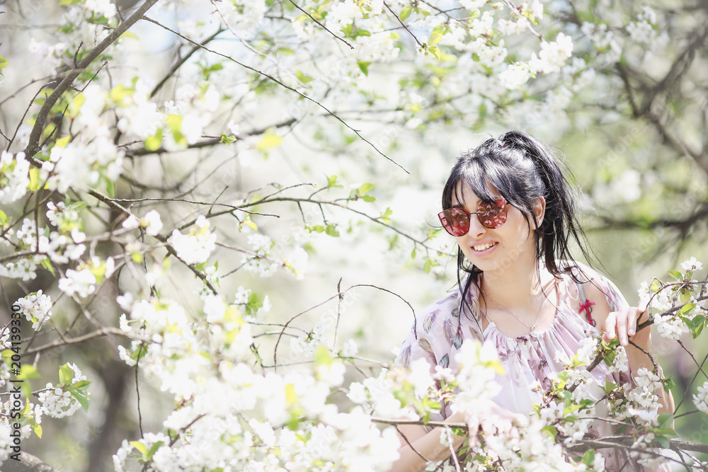 Beautiful brunette girl in a blooming spring garden wearing sunglasses. Beautiful brunette girl in a blooming spring garden wearing sunglasses.