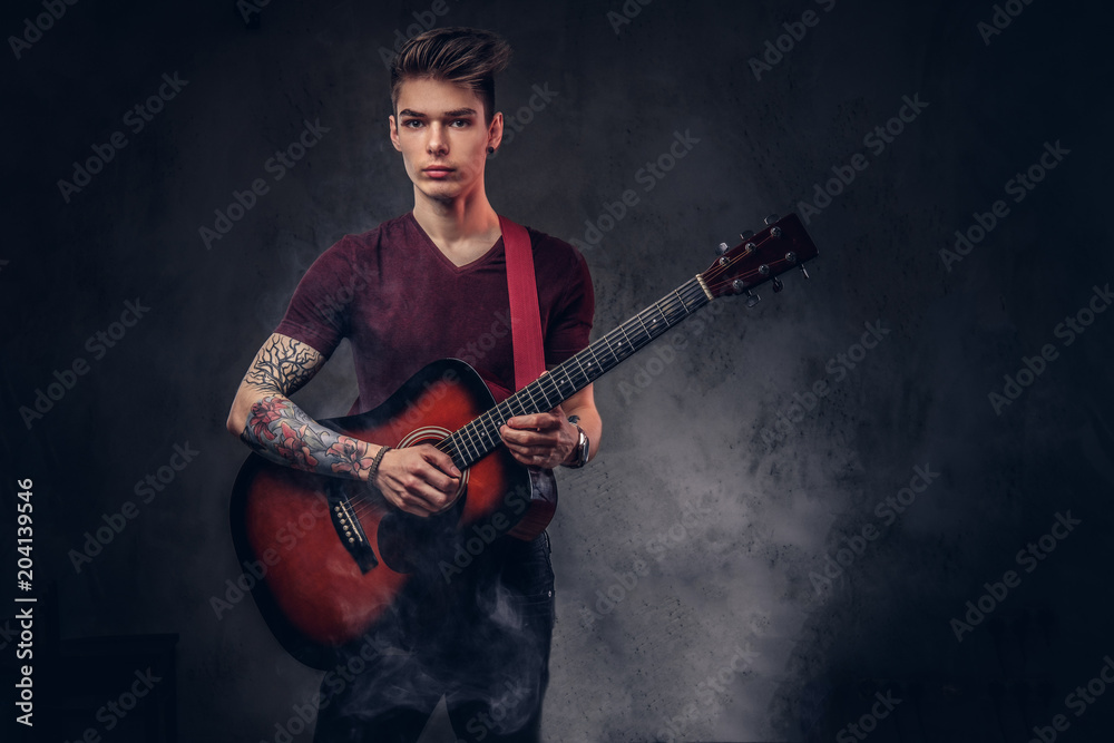 Obraz premium Handsome young musician with stylish hair in a t-shirt, holds a guitar in his hands and playing.