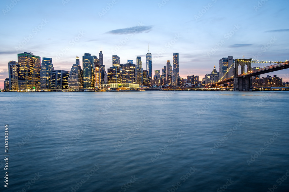 Night view of Manhattan skyline and Brooklyn Bridge on top of the Hudson river. New York City, USA.