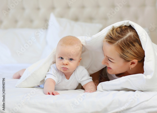 Family portrait of mom and baby in white bed under blanket. The concept of family..