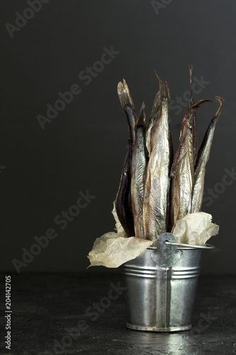 Capelin cold smoked fish in a decorative bucket on a dark background.