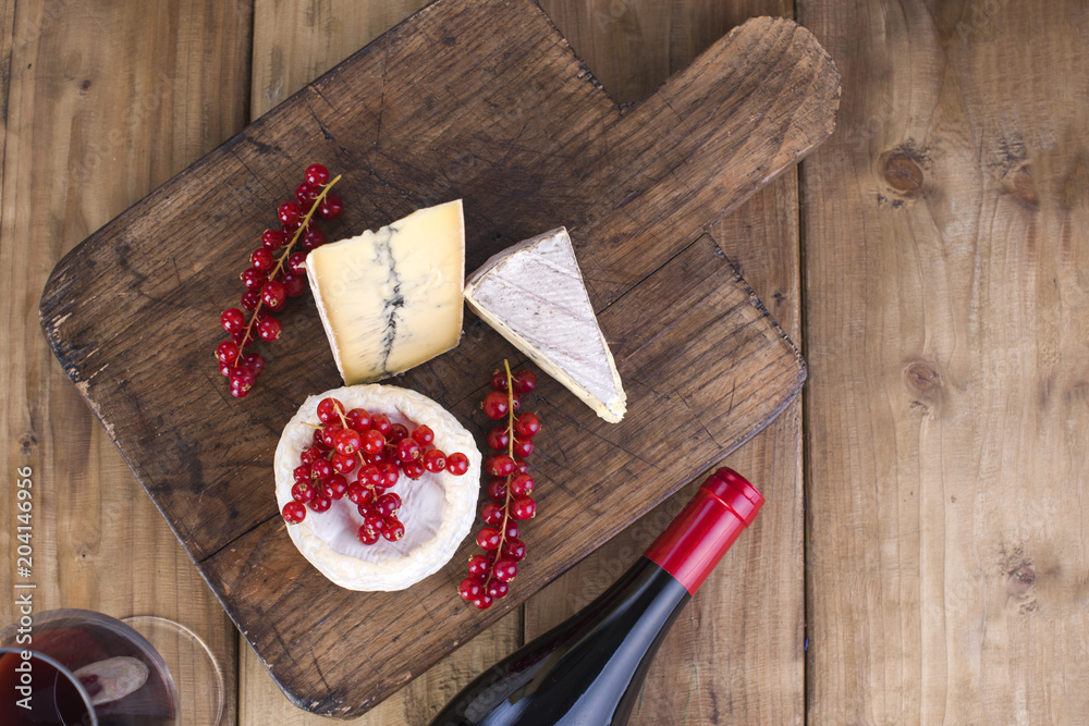 Different cheese with mildew and cream cheese on a wooden board. Red berries. Sauska to wine. Tasty and elegant. Bottle. Place for text. View from above Different cheese with mildew and cream cheese on a wooden board. Red berries. Sauska to wine. Tasty and elegant. Bottle. Place for text. View from above