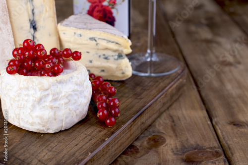 Different cheese with mildew and cream cheese on a wooden board. Red berries. Sauska to wine. A bottle of red wine. Place for text