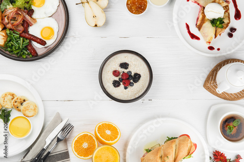 Morning breakfast with muesli, pancakes, fried eggs, bacon, sandwich and tea on white background. Top view.