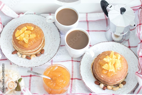 Breakfast for two. American pancakes with orange jam and nuts on vintage plates and 2 white coffee cups. Top view