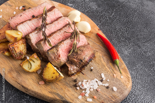 Grilled beef steak with spices, garlic, rosemary and chili pepper on cutting board. Stone background