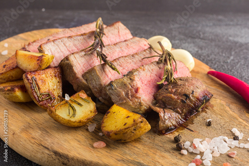 Grilled beef steak with spices, garlic, rosemary and chili pepper on cutting board. Close-up