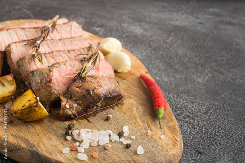 Grilled beef steak with spices, garlic, rosemary and chili pepper on cutting board. Copy space. Stone background