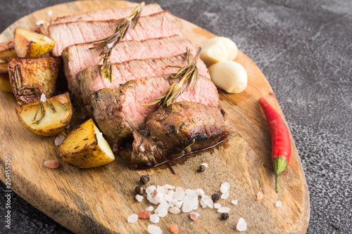 Grilled beef steak with spices, garlic, rosemary and chili pepper on cutting board. Close-up