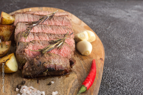 Grilled beef steak with spices, garlic, rosemary and chili pepper on cutting board. Stone background