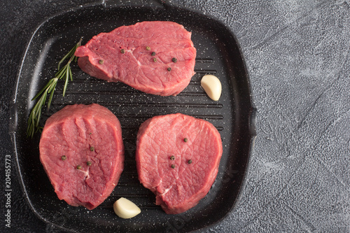 Raw beef meat with rosemary and garlic on a grill pan. Top view