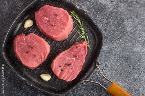 Raw beef meat with rosemary and garlic on a grill pan. Stone background. Top flat view. 