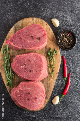 Raw beef meat with rosemary, thyme and chili pepper on a cutting board. Stone background. Top flat view. Vertical view