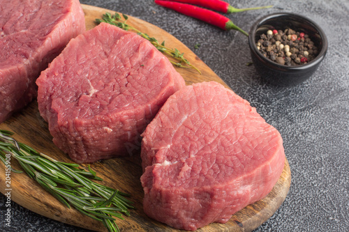 Raw beef meat on a cutting board with rosemary, spices and chili pepper. Gray stone background. Close up
