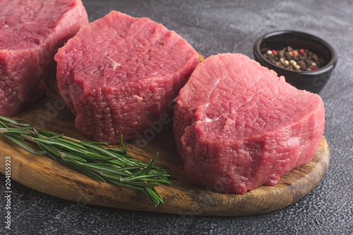 Raw beef meat on a cutting board with rosemary and spices. Gray stone background