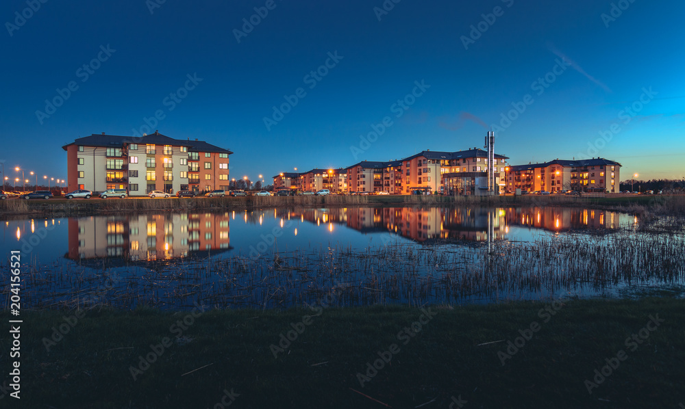 Safe neighborhood with modern apartment buildings at midnight. Area is full of cars and lanterns. Reflection of buildings in the lake. 