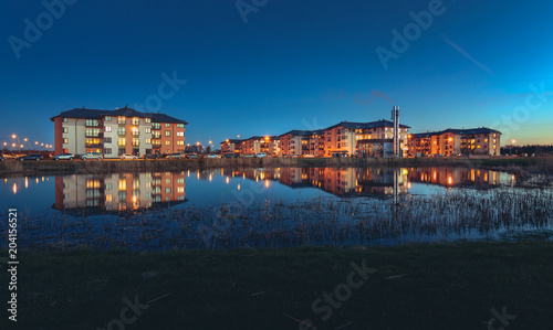Safe neighborhood with modern apartment buildings at midnight. Area is full of cars and lanterns. Reflection of buildings in the lake. 