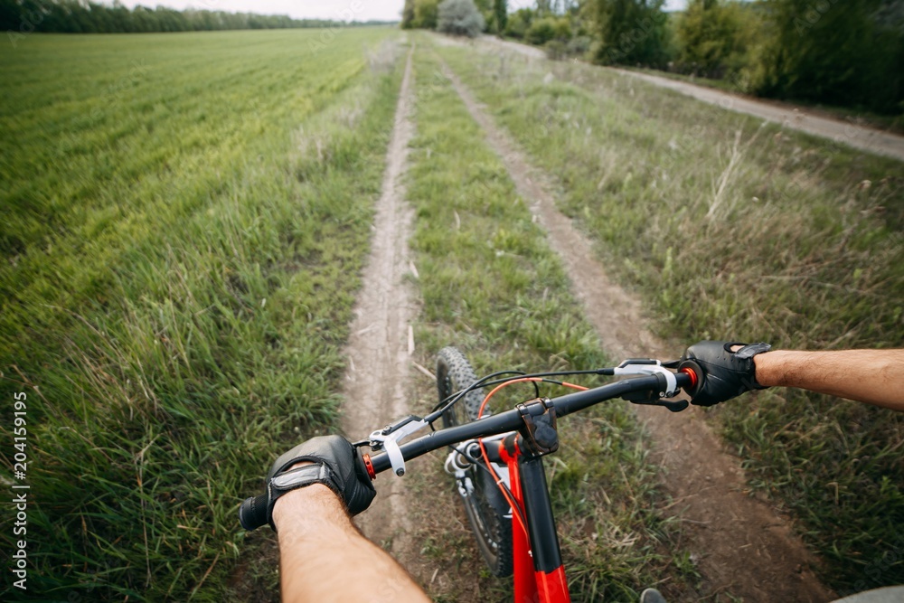 Riding a bike first person perspective with two male hands in gloves holding bicycle handlebar. Sports, tourism and activity concept Riding a bike first person perspective with two male hands in gloves holding bicycle handlebar. Sports, tourism and activity concept
