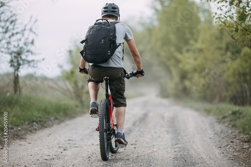 Man in helmet riding a bicycle at country road. Cyclist with backpack traveling. Sports, ecological tourism and activity concept