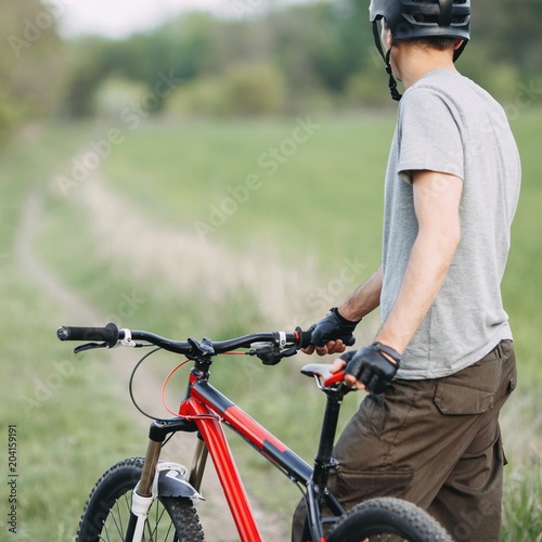 Bicycle sports, traveling, healthy lifestyle and activity. Tourist traveling riding a bike along summer field. Young man in helmet standing with his bicycle getting ready to ride