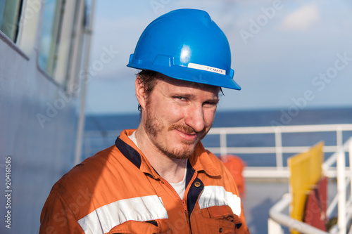 Marine Deck Officer or Chief mate on deck of vessel or ship , wearing PPE personal protective equipment - helmet, coverall. He is looking at camera