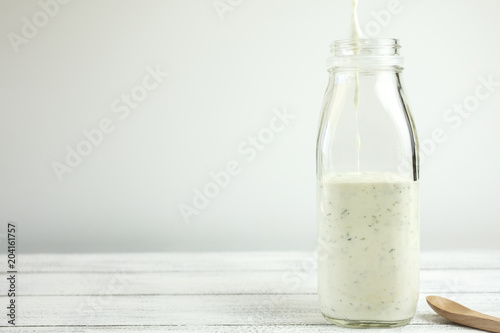 Fotografia Homemade yogurt salad dressing being poured into a milk bottle