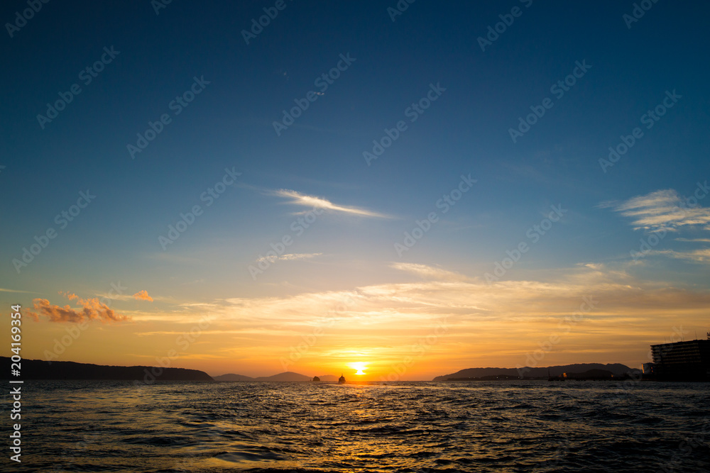 水平線に沈む太陽と島と船
